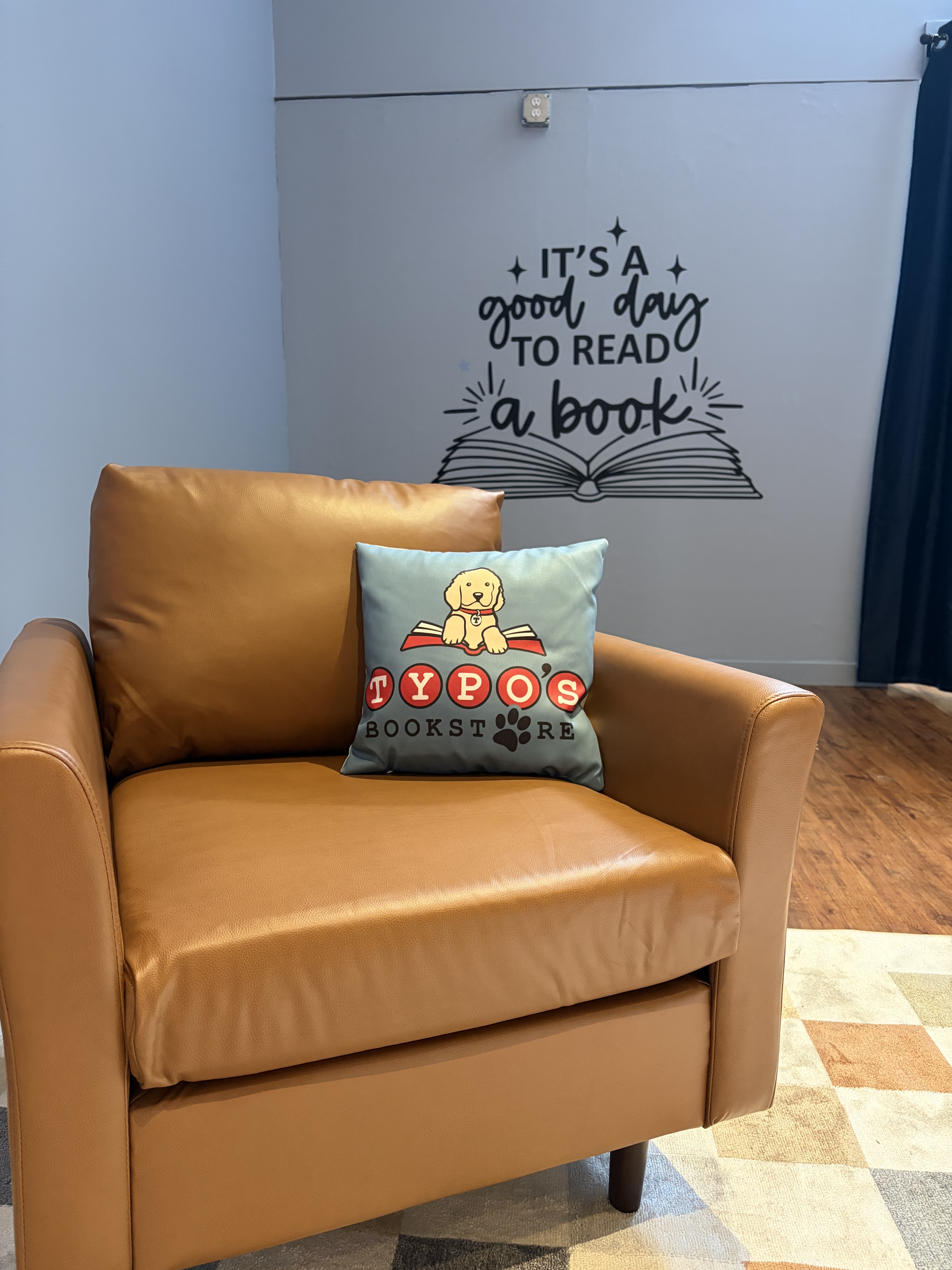 A leather chair with Typo's pillow in front of a sign that says it's a great day to read a book